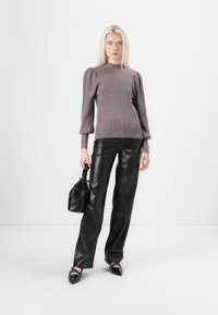 Ribbed knit sweater in mauve with puffed sleeves, paired with high-waisted black leather pants. Holding a small black handbag. Pointed shoes.