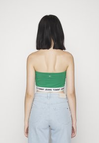 Zelený top bez ramínek s černobandem "TOMMY JEANS", kombinovaný se světle modrými džíny s vysokým pasem. Jednoduché pozadí.