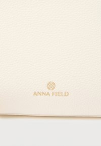 Υφή από δέρμα κρεμ χρώματος με μικρό χρυσό λογότυπο Anna Field και κυκλικό έμβλημα στη μέση κάτω πλευρά.