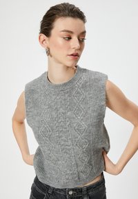 Grauer ärmelloser Strickpullover mit strukturiertem Zopfmuster, rundem Ausschnitt und verkürztem Schnitt, gefertigt aus einem weichen, flauschigen Material.