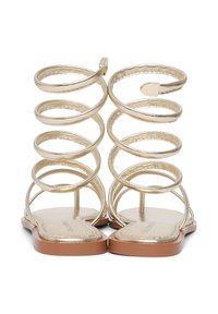 Gold metallic sandals with spiral ankle straps, flat soles, and a brown base. The design features a minimalist open-toe style.