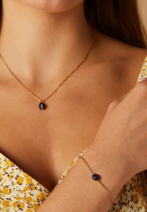 Collier et bracelet en chaîne dorée avec une pierre ovale bleu foncé, mettant en avant un design simple et élégant.