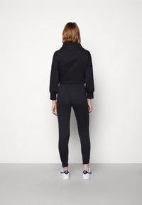 Svart sweatshirt med hög krage och sänkta axlar, kombinerad med svarta leggings. Avslutad med vita sneakers med svarta detaljer.