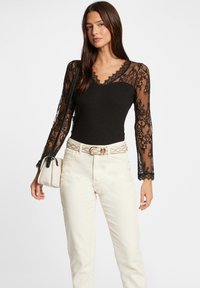 Zwarte bodysuit met lange kanten mouwen en een scalloped halslijn, gecombineerd met witte hoge taille jeans en een kleine beige handtas.