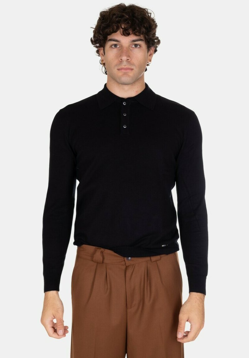 Maglietta polo nera a maniche lunghe con colletto e chiusura a tre bottoni; superficie liscia; abbinata a pantaloni marroni con pince.