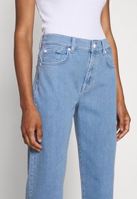 Vaaleansiniset farkut korkealla vyötäröllä, suorat lahkeet ja huomaamattomat ompeluyksityiskohdat; sisältää etutaskut ja vetoketjuluukun.