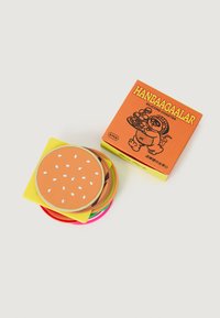 Una pila de posavasos de silicona coloridos, con uno diseñado como un pan de hamburguesa, al lado de una caja naranja etiquetada "HANBAAGAALAR."