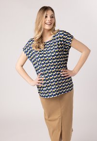 Top blu navy a maniche corte con motivo a scallop giallo e bianco, abbinato a una gonna beige con spacco frontale. Tessuto morbido.
