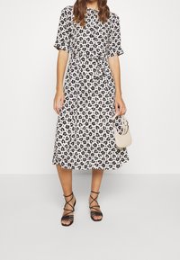 Šaty midi s leopardím vzorem, krátkými rukávy, s úzkým pasem a splývavou sukní; doplněné černými sandály na pásku a malou béžovou kabelkou.