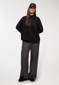 Maglione nero oversize, pantaloni grigi a gamba larga e berretto in pelle nera. Texture morbide con un design minimalista e dettagli discreti.