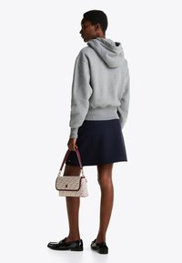 Felpa grigia, gonna navy e mocassini neri. Tiene una borsa a tracolla con una tracolla bordeaux. Sembra casual e moderna.