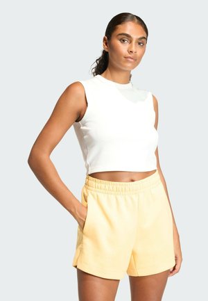 Biały, prążkowany, bezrękawnik crop top w parze z miękkimi, żółtymi szortami z elastycznym pasem. Szorty mają kieszenie i luźny fason.