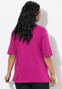 T-shirt magenta a maniche corte realizzato in morbido tessuto, con una vestibilità comoda e fessure laterali per una maggiore libertà di movimento. Vista posteriore mostrata.