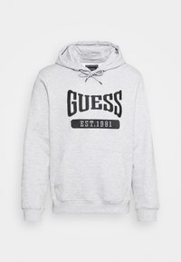 Sudadera gris claro con un bolsillo canguro en el frente, capucha con cordones y el logo negro "GUESS EST.1981" exhibido de manera destacada. Material suave.