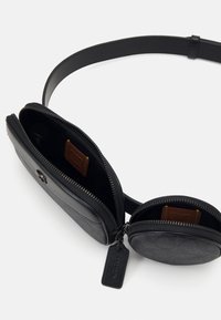 Svart läderväska med en texturerad yta, med ett huvudfack och en cirkulär dragkedjeficka. Inkluderar en tagg och justerbar rem.