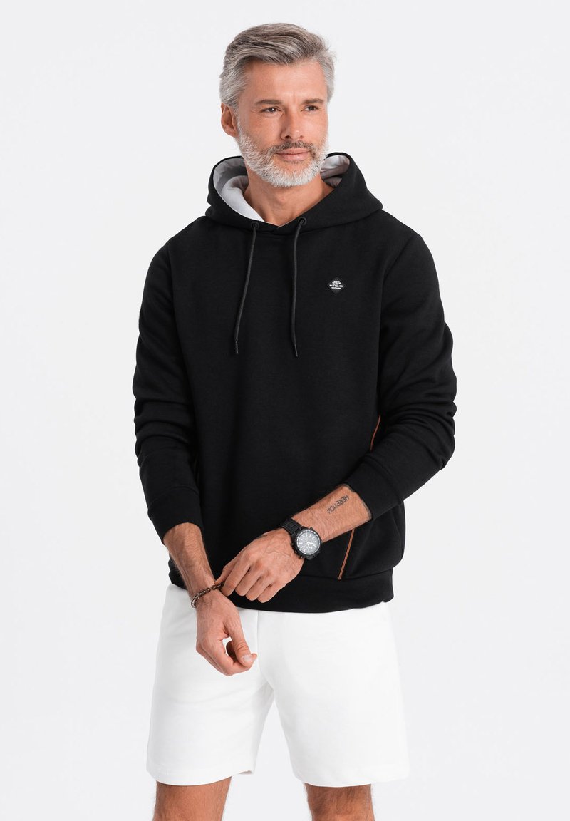 Sudadera negra con forro gris, bolsillo tipo canguro y cordón. Presenta un logo en el pecho y acentos naranjas en el lateral.