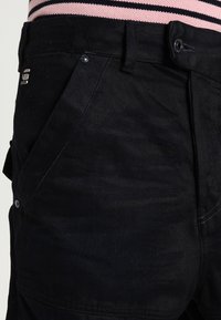 Shorts de mezclilla negra con un frente plano, dos bolsillos laterales y detalles de metal. La tela parece suave y con un ligero brillo.