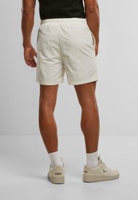 Shorts en crème claire avec une taille élastique, un tissu texturé, des poches latérales et une coupe décontractée, associés à des baskets claires et des chaussettes blanches.