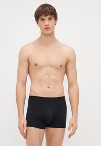 Schwarze Baumwoll-Boxershorts mit solidem Design, enganliegendem Schnitt und breitem elastischen Bund, getragen von einem Model ohne Shirt.