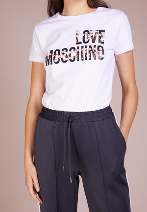 Wit T-shirt met korte mouwen met de tekst "LOVE MOSCHINO" versierd met kleine bloemenprints, gedragen met zwarte broek met trekkoord.