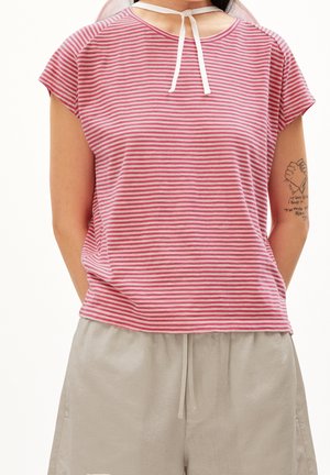 Personne portant une chemise à manches courtes rayée rose et blanche avec un cordon blanc noué au niveau de l'encolure et un pantalon beige clair à taille réglable par cordon.