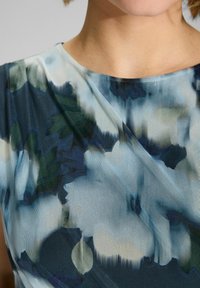 Blumendruckstoff in Schattierungen von Blau und Grün mit einer weichen, strukturierten Oberfläche. Nahaufnahme von Ausschnitt und Schultern.