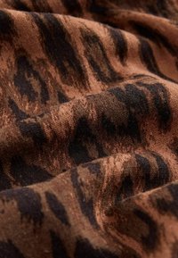 Tissu marron avec motif de rayures de tigre noires, montrant un matériau texturé et doux avec de légers plis et ombres.