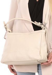 Crème leren handtas met een gestructureerde vorm, verstelbare schouderriem en subtiele stiksels. Gladde textuur, minimale hardware.