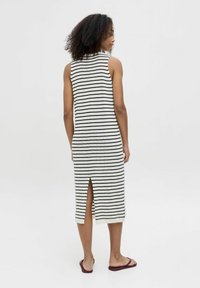 Vestido de punto con rayas verticales en blanco y negro, diseño sin mangas, detalle de abertura en la espalda y escote redondo. Llevado con sandalias planas.