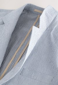 Triibuline puuvillane bleiser, helesinine ja valge, millel on sälguga krae, pehme vooder ja küljetasku detail.