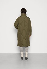 Olive green puffer coat with a high collar, diamond quilted pattern, mid-length design, paired with patterned trousers and cream-colored boots.