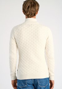 Stickad tröja i krämfärg med diamantmönster, ribbad krage och muddar, med en strukturerad yta och slimmad passform.