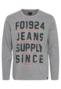 Grå langærmet t-shirt lavet af blødt stof med store sorte og orange bogstaver. Rund halsudskæring og afslappet pasform.