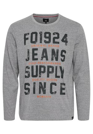 Hallikas pika varrukaga T-särk pehmest kangast, millel on suured mustad ja oranžid kirjad. Ümar kaelus ja mugav lõige.