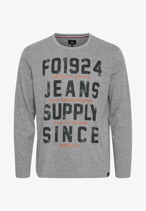 Hallikas pika varrukaga T-särk pehmest kangast, millel on suured mustad ja oranžid kirjad. Ümar kaelus ja mugav lõige.