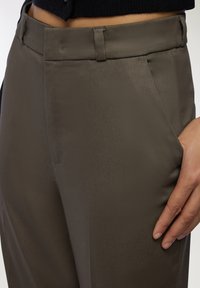 Pantaloni marroni su misura con una texture liscia, dotati di tasche frontali e taglio dritto. Il tessuto ha una leggera lucentezza.