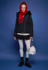 Črna podložena jakna s krznom na robu, rdeč šal, beli pulover, črno krilo z volančki, bele nogavice, črni škornji, drži puhasto belo torbico.