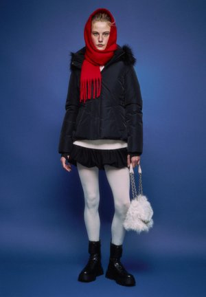 Črna podložena jakna s krznom na robu, rdeč šal, beli pulover, črno krilo z volančki, bele nogavice, črni škornji, drži puhasto belo torbico.