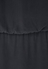 Svart texturerad tyg med en mjuk känsla, med en rynkad sektion vid midjan och en slät, flödande hängning nedanför.