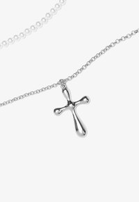 Pendentif croix en métal argenté sur une fine chaîne. La croix a une surface lisse et polie, avec des extrémités arrondies et une légère courbe.