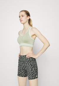 Sutiã de desporto verde claro com detalhes brancos e texturizados, combinado com calções pretos com um padrão abstrato ousado em verde e branco.