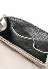 Beige kožená taška uvnitř se zipem, s šedým podšívkovým vzorem ve tvaru cik-cak a jednou velkou kapsou, která má dvě menší části.