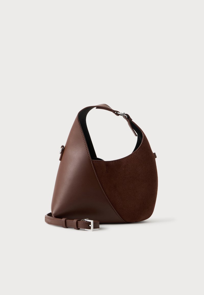 Sac à bandoulière bicolore en cuir marron avec un devant en daim courbé, une sangle ajustable et une boucle argentée, présenté sur un fond uni.
