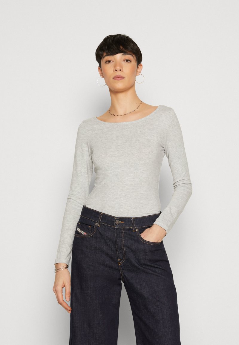 Top de manga larga gris claro hecho de tela suave, con un cuello ancho. Combinado con pantalones de mezclilla oscuros de pierna ancha con bolsillos frontales.