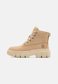 Bottines en daim beige à bout rond, œillets en métal, lacets crème, semelle épaisse beige et logo embossé sur le côté.