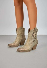 Bottes de cowboy en cuir tan avec un bout pointu, un talon angulé et une broderie décorative en motif zigzag. Zips latéraux pour un enfilage facile.