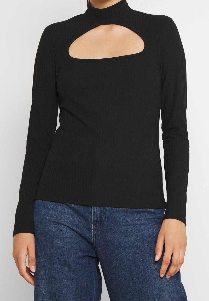 Maglia nera a coste con maniche lunghe e collo alto, caratterizzata da un grande ritaglio rettangolare al petto e una silhouette aderente.