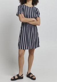 Navy blue dress with pink vertical stripes, short sleeves, round neck, and flared skirt. Worn with black sandals featuring thick straps.