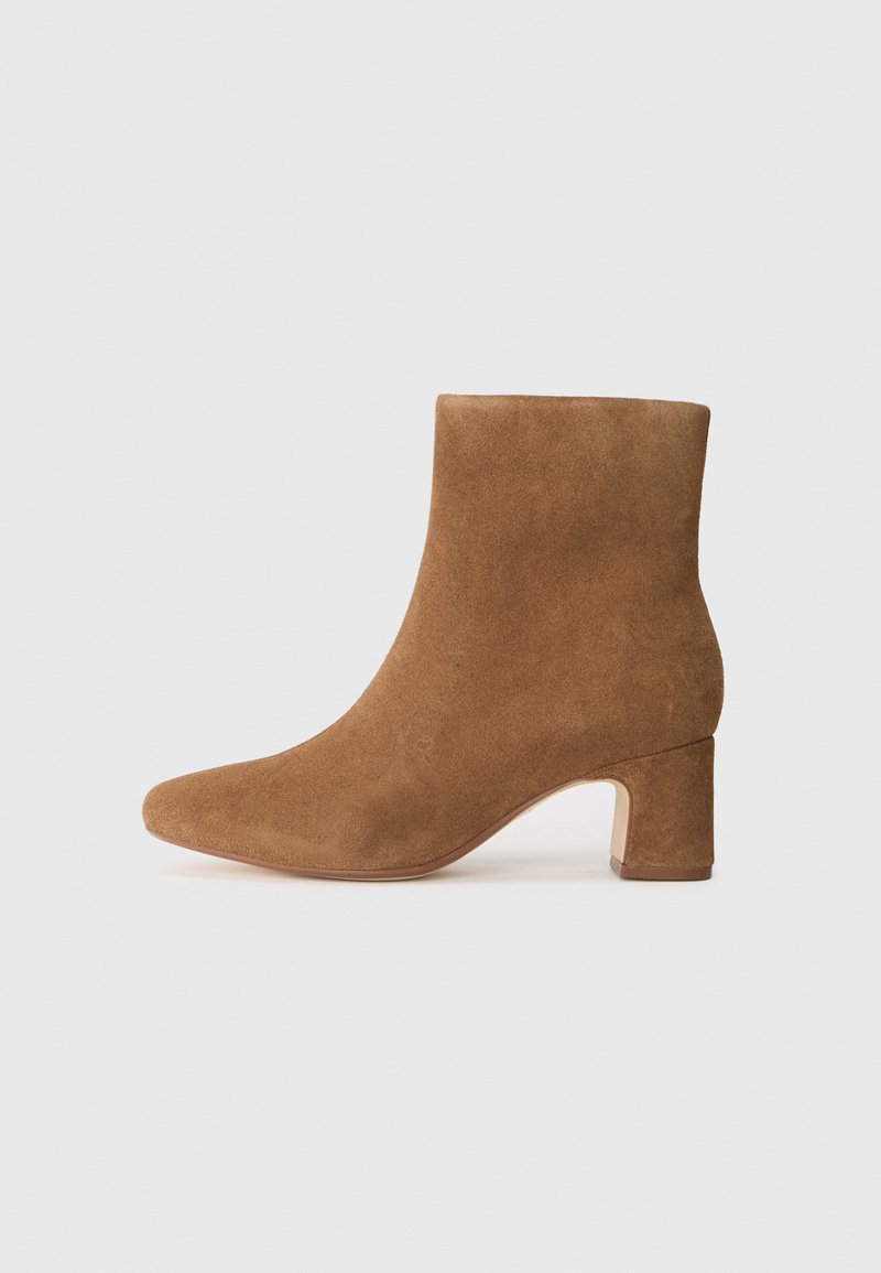 Bota de tobillo de ante marrón con punta afilada y tacón cuadrado, textura suave y silueta ajustada.