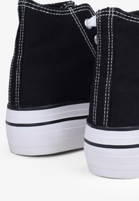 Le sneakers alte in tela nera presentano cuciture bianche, lacci rotondi e una suola in gomma bianca con una striscia nera.